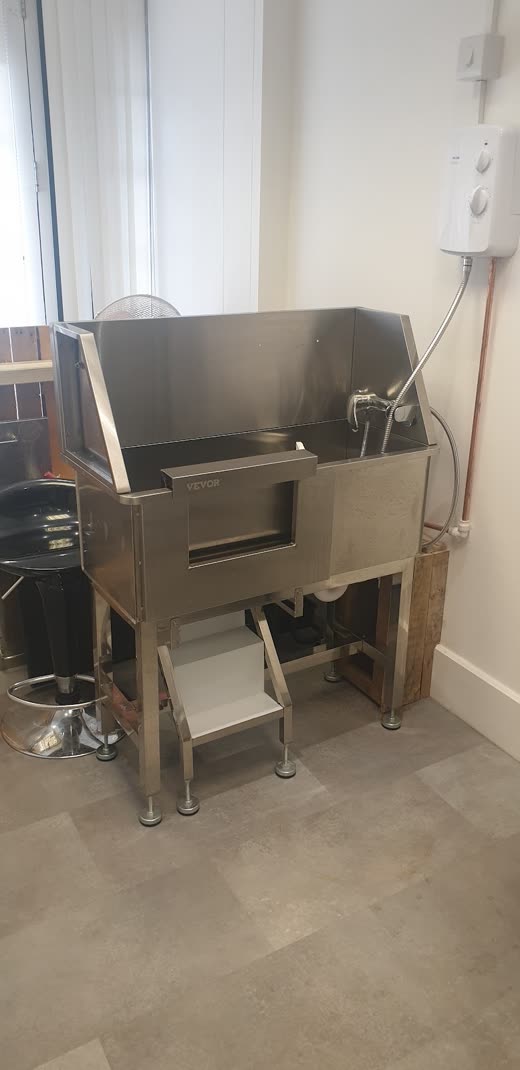 A stainless steel dog bath with a step-up ramp in a tiled grooming room